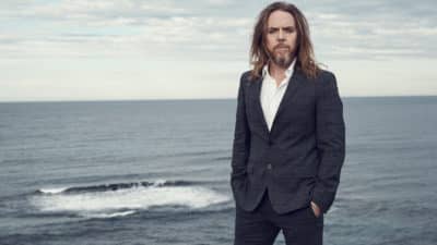 Tim minchin livestream concert image featuring tim standing in front of the ocean, photographed by Damian Bennett