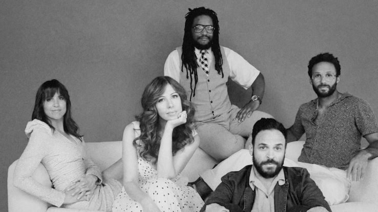 This black-and-white image shows five people sitting on a couch. The central woman rests her head on her hand, while the others sit casually around her, creating a relaxed yet thoughtful scene.